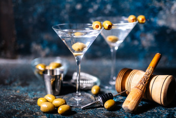 Martini cocktail drink with olives garnish and tools on rusty background