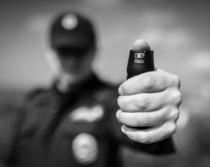 Detail of a police officer holding pepper spray. Selective focus with shallow depth of field. Black and white toning.