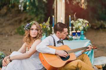 Romantic couple sitting outdoors at sunset with the man playing