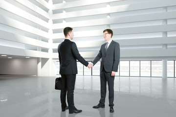 Businessmen shake hands in empty hall of business center