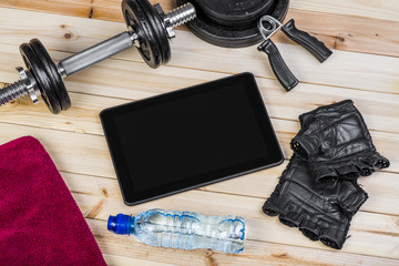 Sport Equipment. Dumbbells, Free Weights, Barbell, Hand Grip, Sport Gloves, Towel, Bottle Of Water And Digital Tablet To Workout Plan On Wooden Boards. Sport Fitness Background