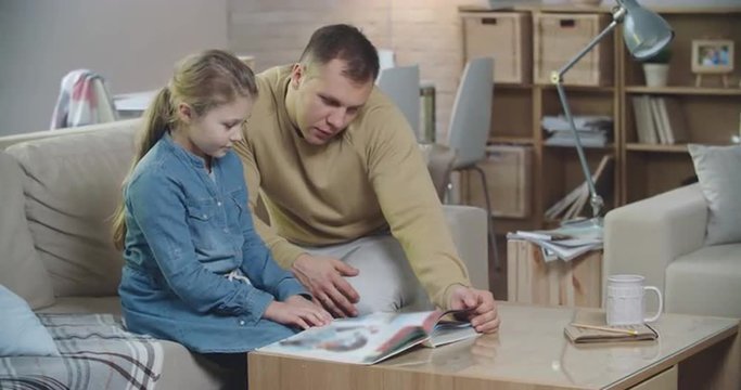 Dad reading book with his little daughter in the living room