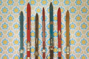 Fototapete Vintage colorful used skis in front of retro wallpaper © Martin Bergsma