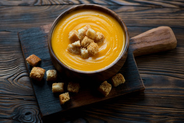 Pumpkin cream-soup with croutons in a dark rustic wooden setting