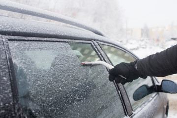 man cleans snow from car window
