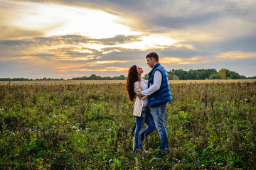 Naklejka na ściany i meble Young couple holding hands in a meadow at sunset