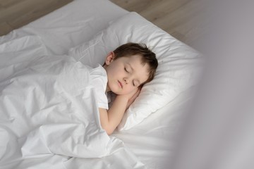 Adorable boy sleeping in bed, happy bedtime in white bedroom