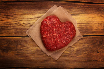 Raw heart shaped burger cutlet over grunge wooden background. Top view. Toned image