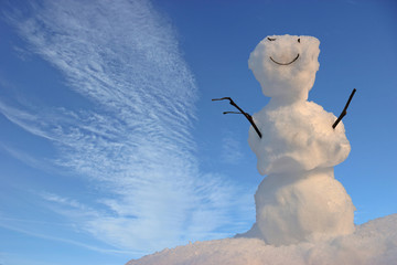 Freundlicher kleiner Schneemann vor blauem Himmel mit weißen Wolken 
