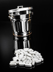 Expired white pill and metal trash on black background with reflection