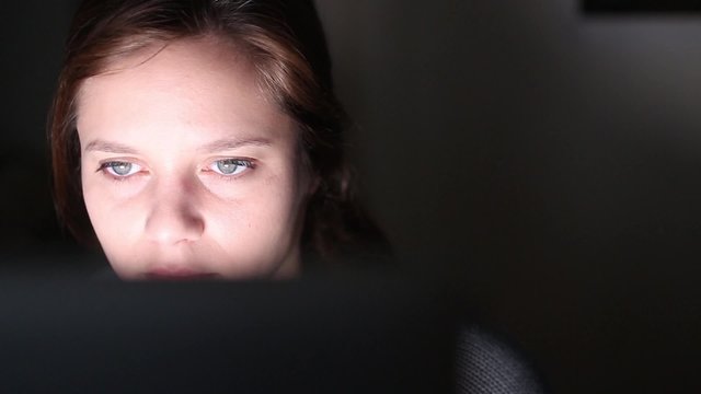 Computer screen reflected in woman's face at night. Girl using computer at night with screen reflected on her face. Pan camera - 1080p