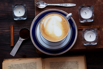 Coffee composition with old book, white tea candles, silver spoon, ground coffee and cinnamon on...