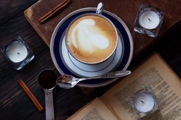 Coffee composition with old book, white tea candles, silver spoon, ground coffee and cinnamon on...
