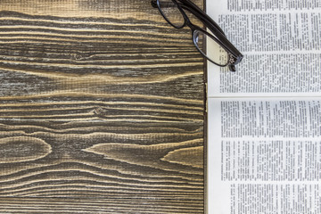 An open empty book and eyeglasses are  on a wooden background. Top view