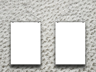 Close-up of two hanged paper sheets with clothes hangers on rough concrete wall background