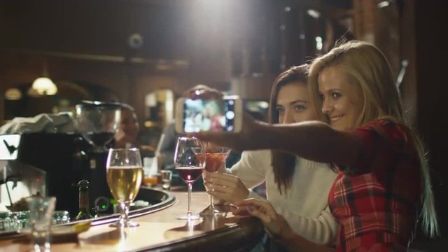 Two beautiful girls are doing selfies on a smartphone while having a good time in a bar. Shot on RED Cinema Camera.
