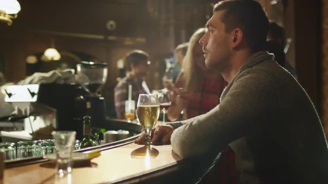 Timelapse footage of a man sitting alone with beer in a bar while people are having good time. Shot on RED Cinema Camera.