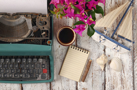 image of vintage typewriter, blank notebook, cup of coffee and old sailboat on wooden table