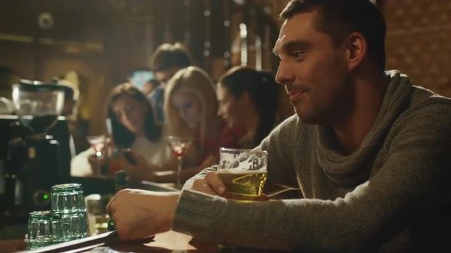 Attractive man is drinking lager beer in a crowded pub. Shot on RED Cinema Camera.