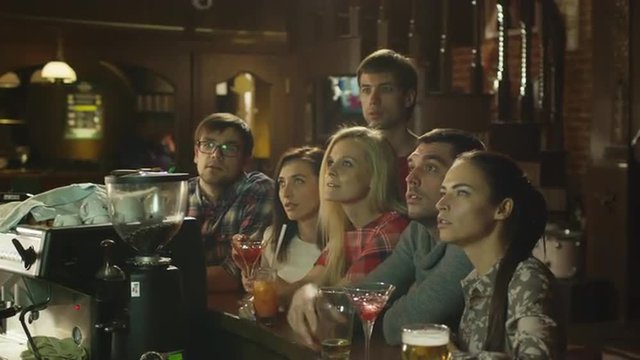 Friends are sitting with drinks and watching a sports game in a bar. Shot on RED Cinema Camera.