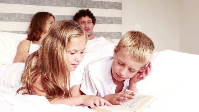 Siblings reading book on bed