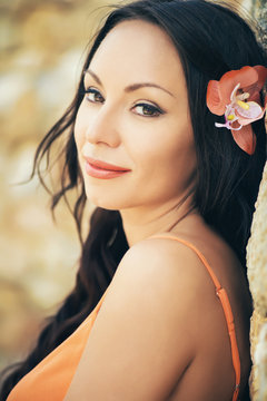 Beautiful portrait of a young brunette woman with orange flower in her hair. Smiling face
