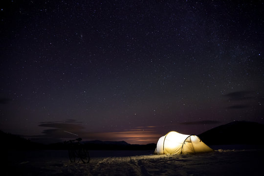     beleuchtetes Zelt im Winter in Schweden mit leichten Nordlichtern im Hintergrund 