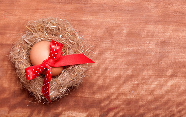 egg swollen by a red bow lies in the nest on the wooden backgrou