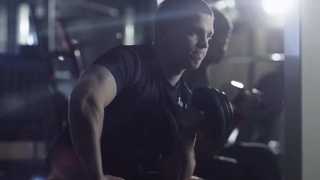 Handsome fit sporty man is exercising with heavy dumbbell in the gym. Shot on RED Cinema Camera.