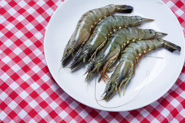 raw black tiger prawns on a plate on red white tablecloth, view