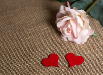 Two red hearts and a rose piece of fabric. The flower is blurred on purpose to keep the focus on the two red hearts