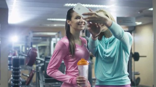 Two attractive fit sporty girls are making selfie pictures on mobile phone in the gym. Shot on RED Cinema Camera.