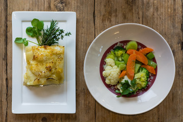 Dauphinois potato with steamed vegetables, from above. Classic French vegetable dishes, with garnish on white plates
