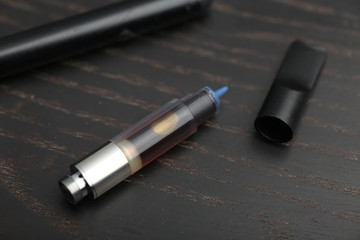 Cannabis oil dispenser/electronic cannabis oil vaporizer with oil-filled cartridge on wood surface