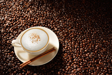 Cup of cappuccino and cinnamon on coffee beans