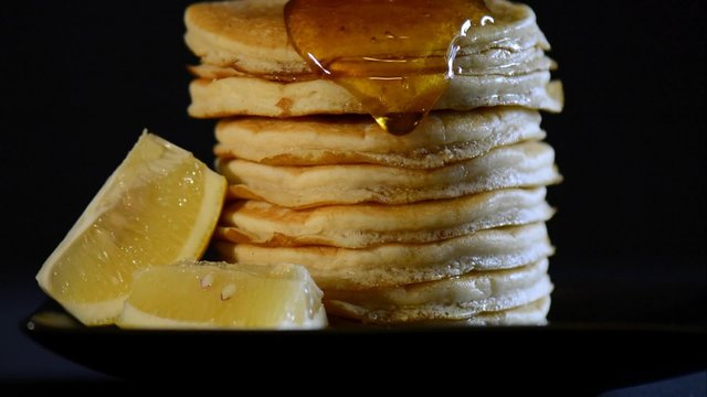 Shrove Tuesday breakfast with honey syrup pouring over the side of tall stack of pancakes, closeup.
