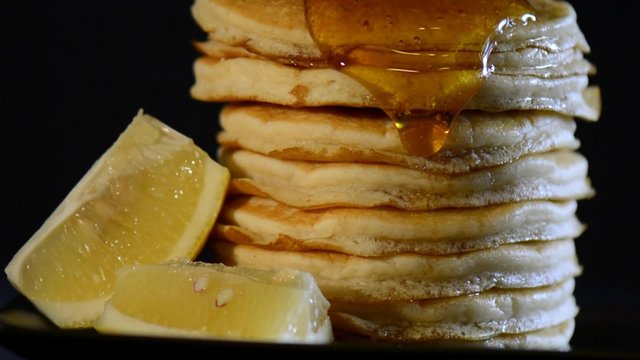Shrove Tuesday breakfast with honey syrup pouring over the side of tall stack of pancakes, zoom.