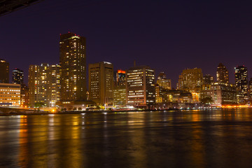 Manhattan skyscrapers with colorful reflections in East River at night. A view on Manhattan from Roosevelt Island at night in New York, USA.