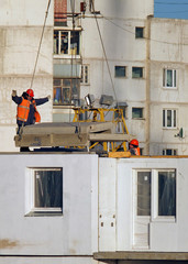 Строительство нового жилого дома. Рабочие принимают поднятую башенным краном на этаж плиту