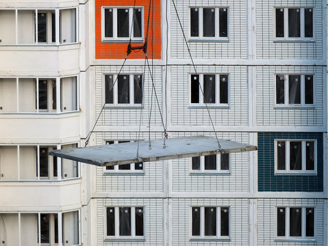 Кран поднимает строительную плиту по воздуху на фоне этажей новостройки на строительстве жилого дома