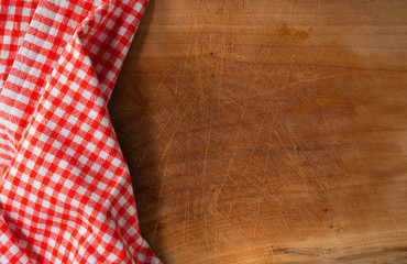 Fototapeta na wymiar Cutting Board Covered with Tablecloth / Used wooden cutting board partially covered with a red and white checkered tablecloth