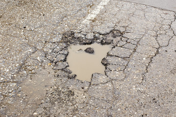 A road damaged by rain and snow, that is in need of maintenance. Broken asphalt pavement resulting in a pothole, dangerous to vehicles.
