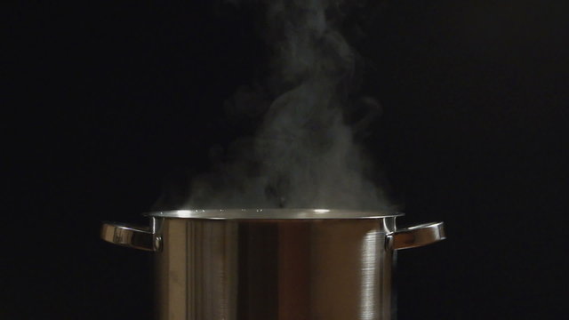 SLOW: A steam lifts up over a steel pan on a black background
