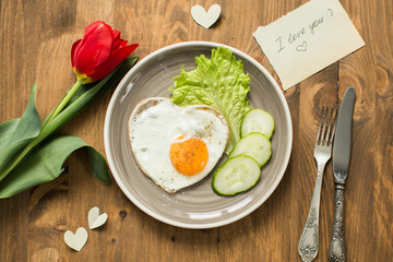 Breakfast on Valentine's Day - fried eggs in the shape of a heart and fresh vegetables. 