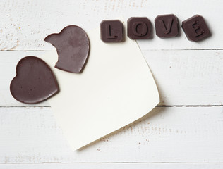 Chocolate heart with note paper on the wooden background