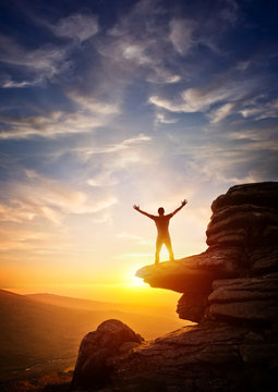 A person reaching up from a high point, set against a sunset. Expressing freedom