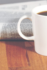 A black coffee with newspaper. Image taken on a wooden table and has a vintage effect applied.