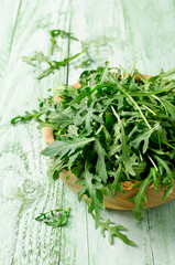 Fresh green arugula in bowl on wooden table