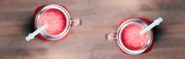 A top shallow dof view of a watermelon smoothies in a mason jars with tubes on wooden background. Selective focus on tubes