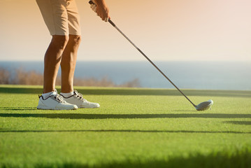 Golfer is going to tee off at sunset, ocean and horizon